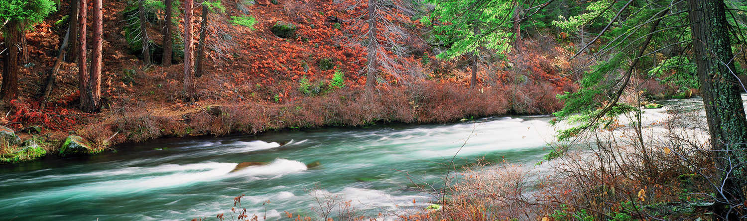 a flowing river with red fall colors of trees around it